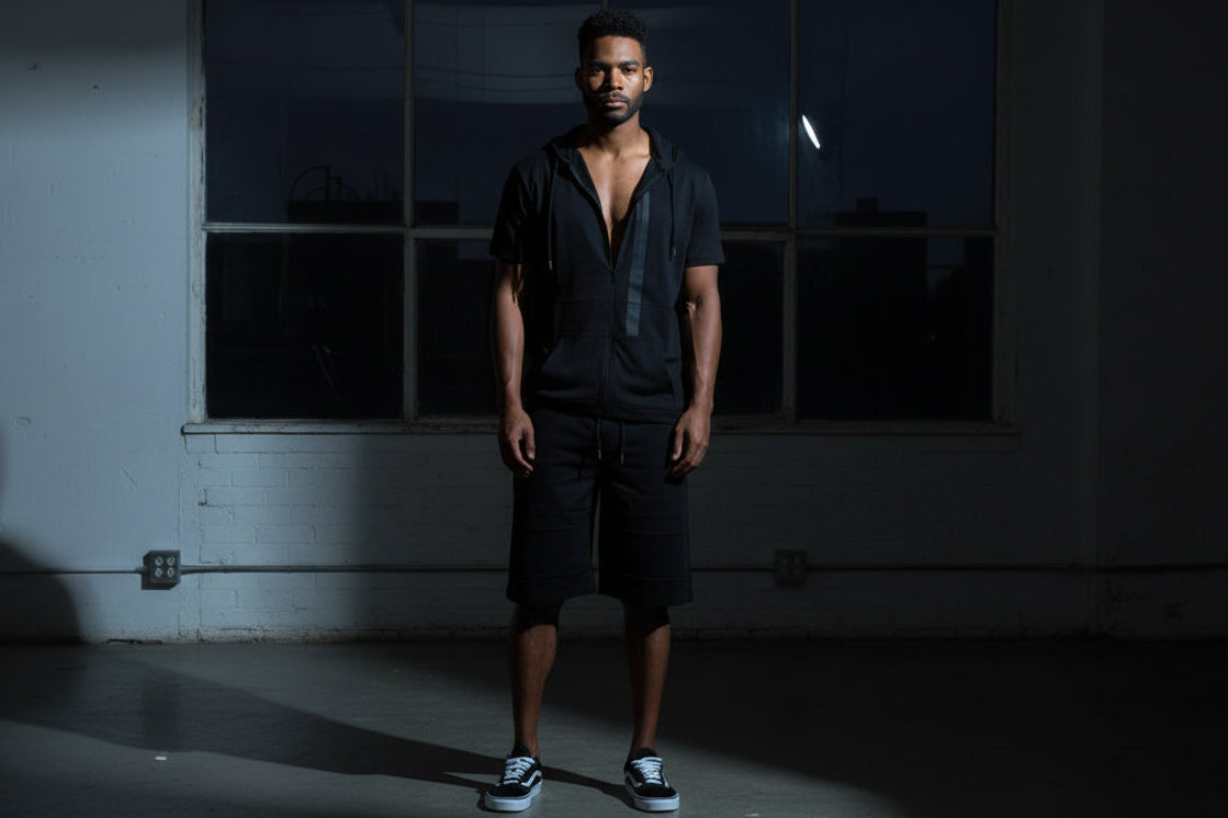 Man wearing a black outfit with a hood on a urban studio background