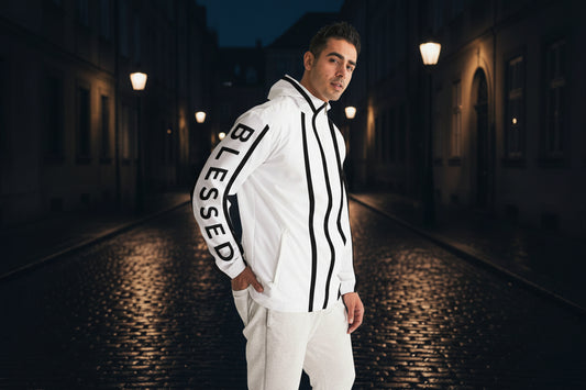 Man wearing a white jacket with 'BLESSED' text on a cobblestone street background with a backlit street showing contrast.