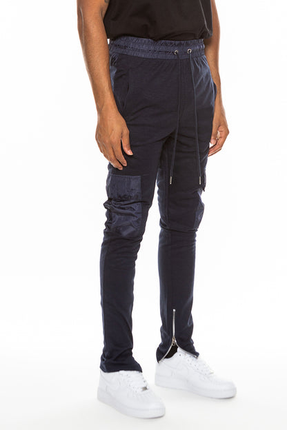 Person wearing dark blue pants with zippers and pockets on a white background